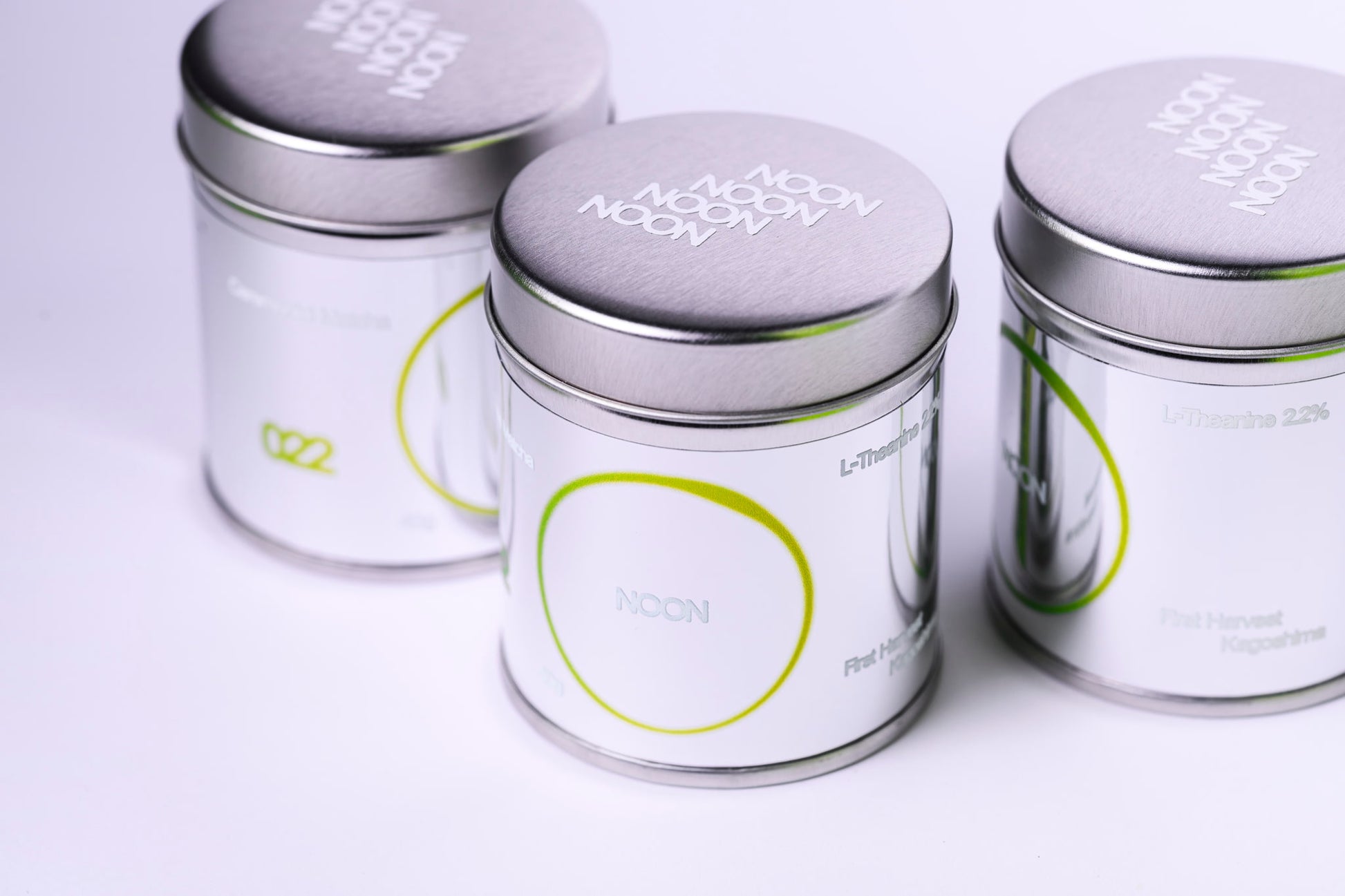 Trīs ceremoniālā matcha bundžas ar NOON etiķetēm uz balta fona