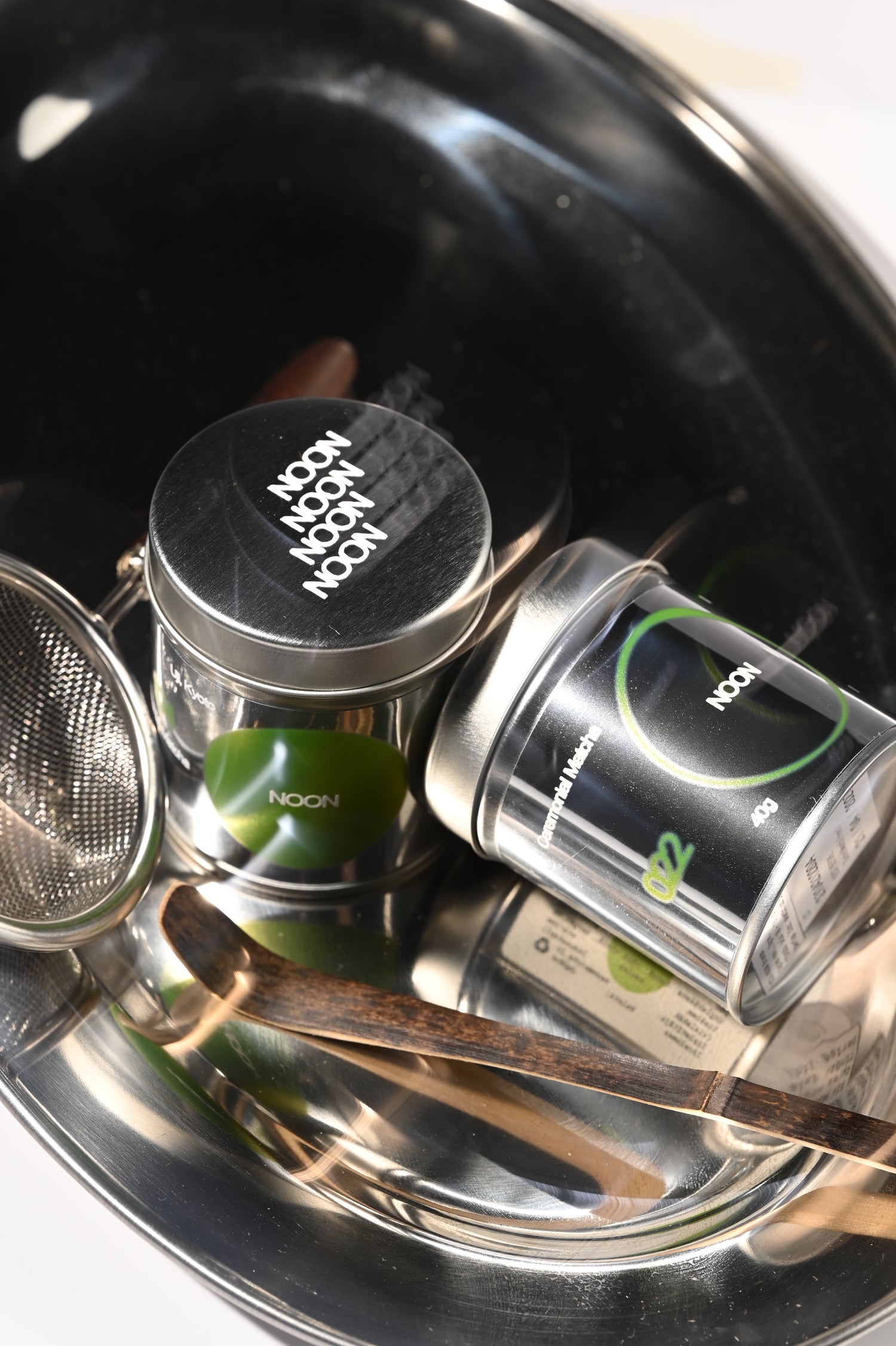104 un 022 matcha bundžas, bambusa karote un sietiņš uz metāliskas paplātes